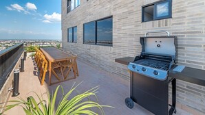 Terraza en la azotea con una parrilla, una mesa de madera y sillas.