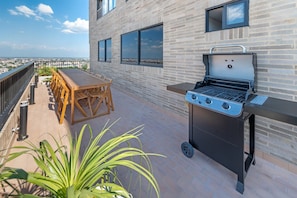 A rooftop patio with a barbecue grill, a wooden table, and chairs. - Edificio Habitare Cristales (Cali)