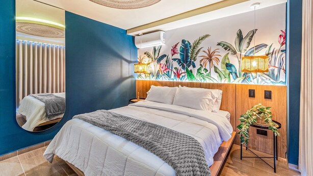 Un dormitorio moderno con una cama grande, aire acondicionado de pared y un mural con motivos tropicales.