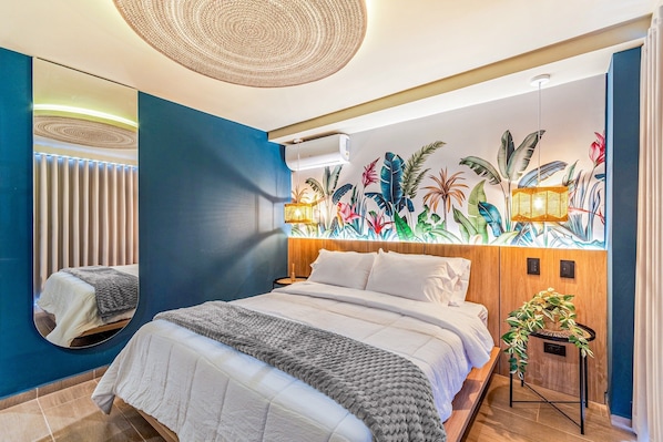 A modern bedroom with a large bed, a wall-mounted air conditioner, and a tropical-themed mural. - Edificio Habitare Cristales (Cali)