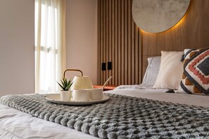 A neatly made bed with a fluffy grey blanket, a bedside table with a lamp, and a tray with cups and a plant. - Edificio Habitare Cristales (Cali)