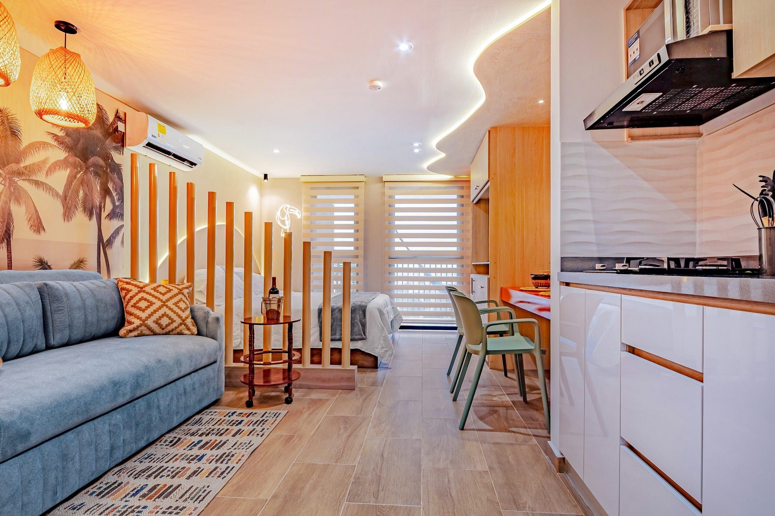 Uma cozinha moderna com fogão embutido, uma sala de jantar com mesa e cadeiras, e uma sala de estar com sofá e almofadas decorativas.