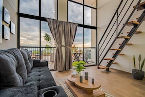 A modern living room with a grey sofa, a wooden coffee table, and a view of the sky through large windows. - Edificio Habitare Cristales (Cali)