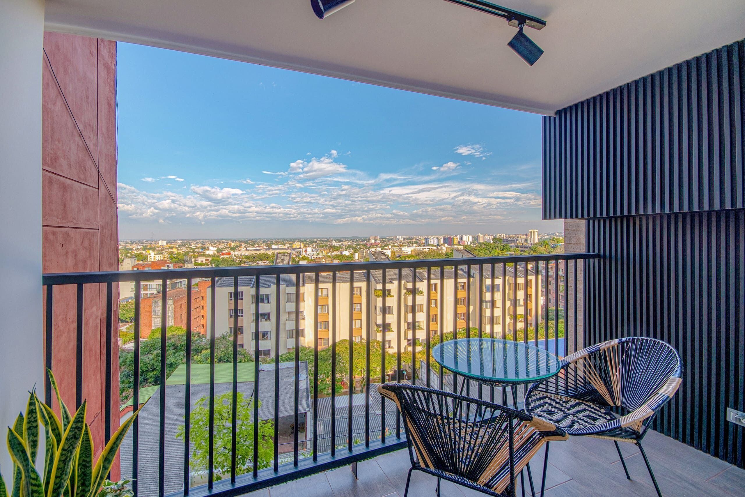 A balcony with a view of a cityscape, two chairs, and a table.