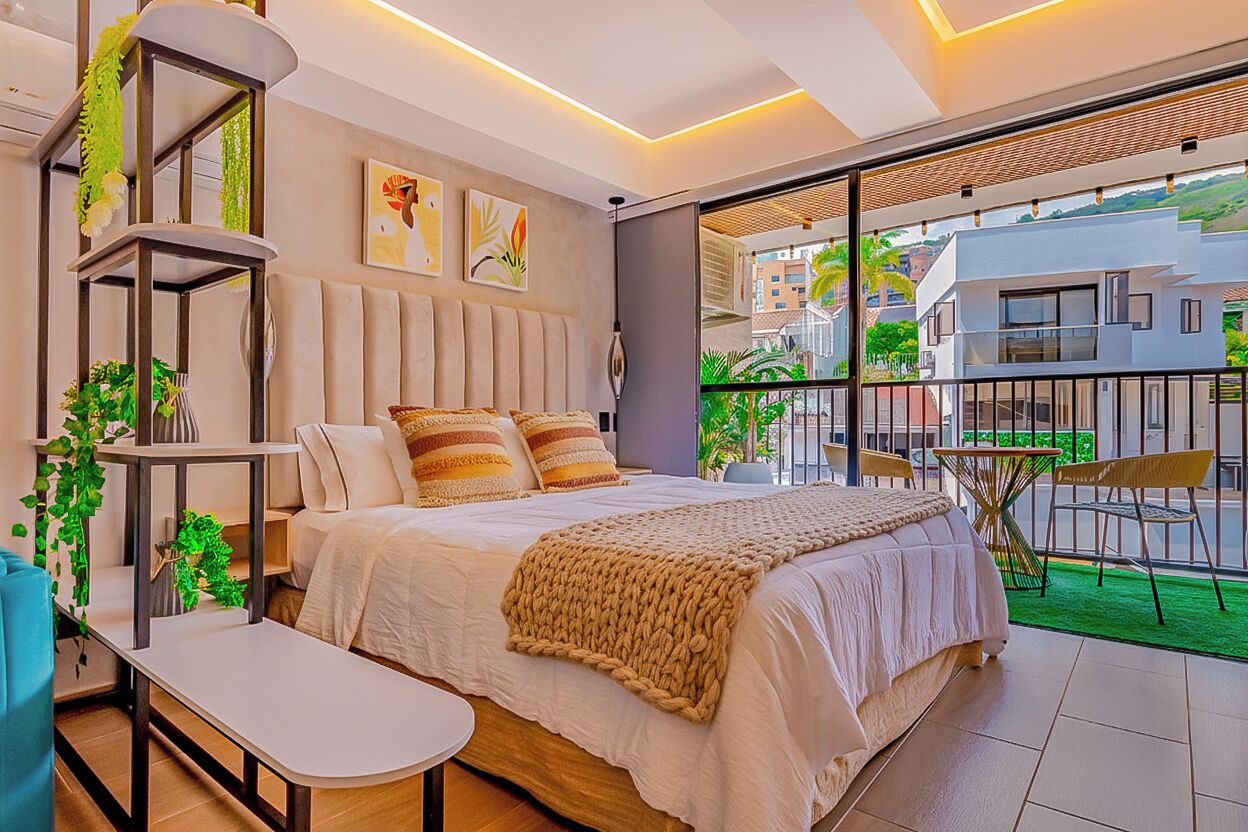 A modern bedroom with a bed, bedside tables, a small table, and a balcony with a view of buildings.
