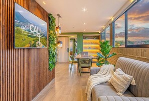 Un'accogliente hall d'hotel moderna con un grande schermo televisivo, una poltrona, un'area ristoro e vista sul paesaggio.