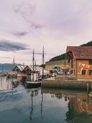 A harbor with boats, a wooden building with a red roof, and a dock with people.