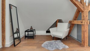 Una stanza con una sedia bianca, uno specchio con cornice nera, un piccolo tavolo con oggetti decorativi e un tappeto morbido su pavimento in legno.