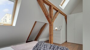 Una camera da letto con soffitto a falde, travi in legno, un letto con coperta, un comò e un armadio.