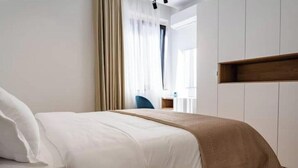 Ett hotellrum med en säng, en hylla i trä och ett fönster med gardiner.