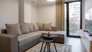 Ein modernes Wohnzimmer mit einer Couch, einem kleinen runden Tisch, einer Pendelleuchte, einer Schiebetür aus Glas und Blick auf Gebäude im Freien.