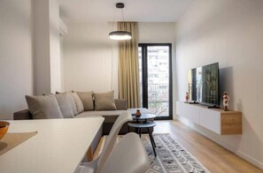 Un salon moderne avec un canapé, une table à manger, un téléviseur fixé au mur et un tapis à motifs.