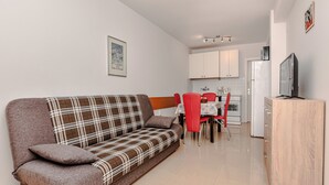 Uma sala de estar moderna com sofá, cadeiras vermelhas, uma mesa de jantar, televisão e área de cozinha.