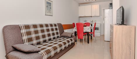 Un salon moderne comprenant un canapé, des fauteuils rouges, une table à manger, un téléviseur et un coin cuisine.