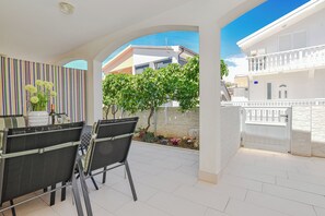 A patio with a table and chairs, a striped wall, and a view of a building with a balcony. - Apartment Bokan (Vir)