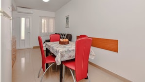 Uma sala de jantar com uma mesa posta para quatro pessoas, cadeiras vermelhas, uma cabeceira de madeira e uma porta branca com janela.