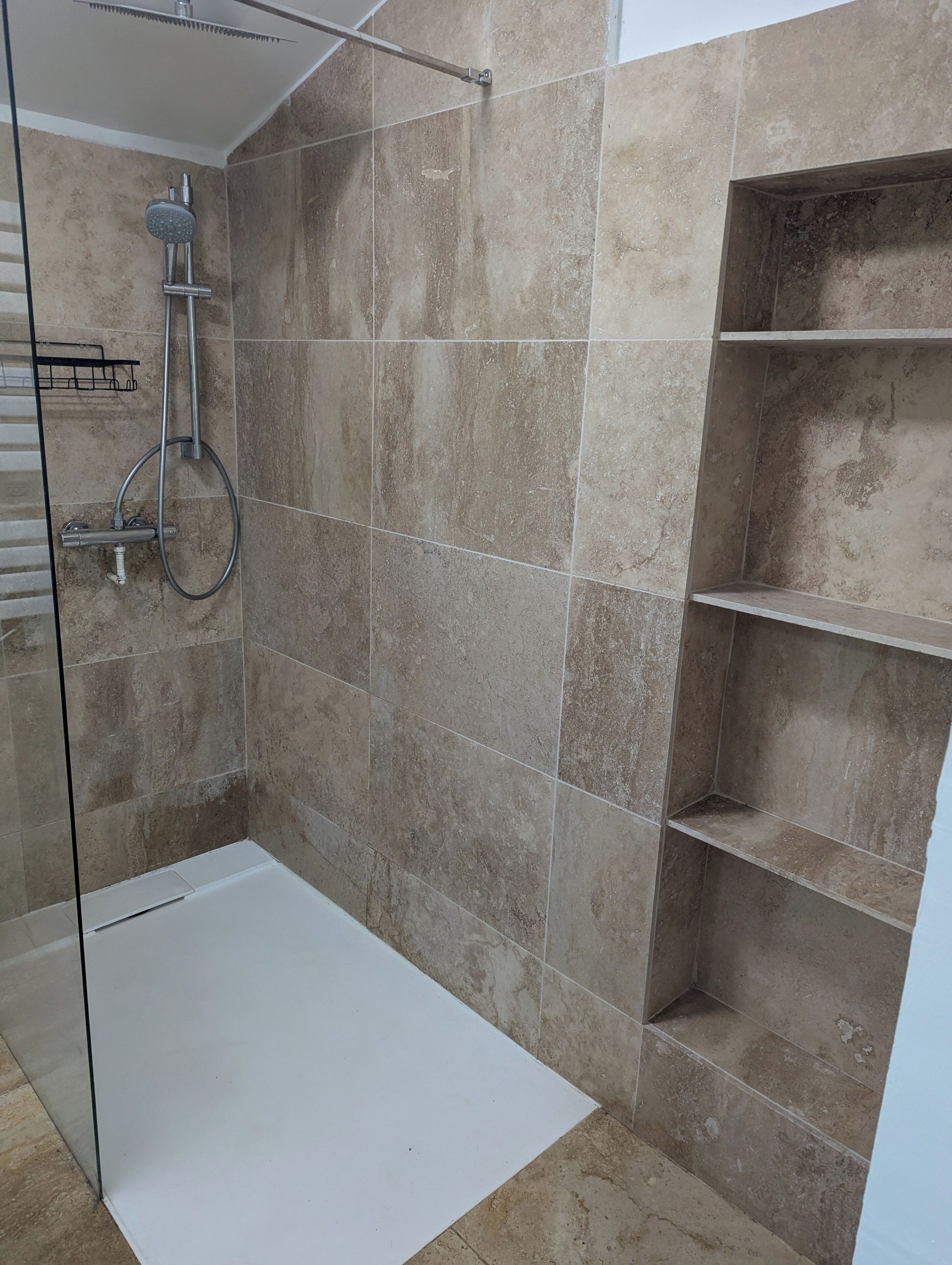 A shower area with a glass door, a handheld showerhead, and a wall-mounted faucet.