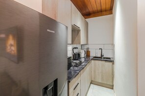 A compact kitchen with a stainless steel refrigerator, wooden cabinets, a countertop with a coffee maker, and a sink.