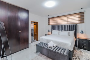 A bedroom with a large bed, bedside tables, a wardrobe, and a door leading to another room.