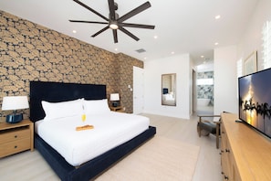 Een moderne slaapkamer met een groot bed, een plafondventilator, een televisie en een zichtbare badkamer door een geopende deur.
