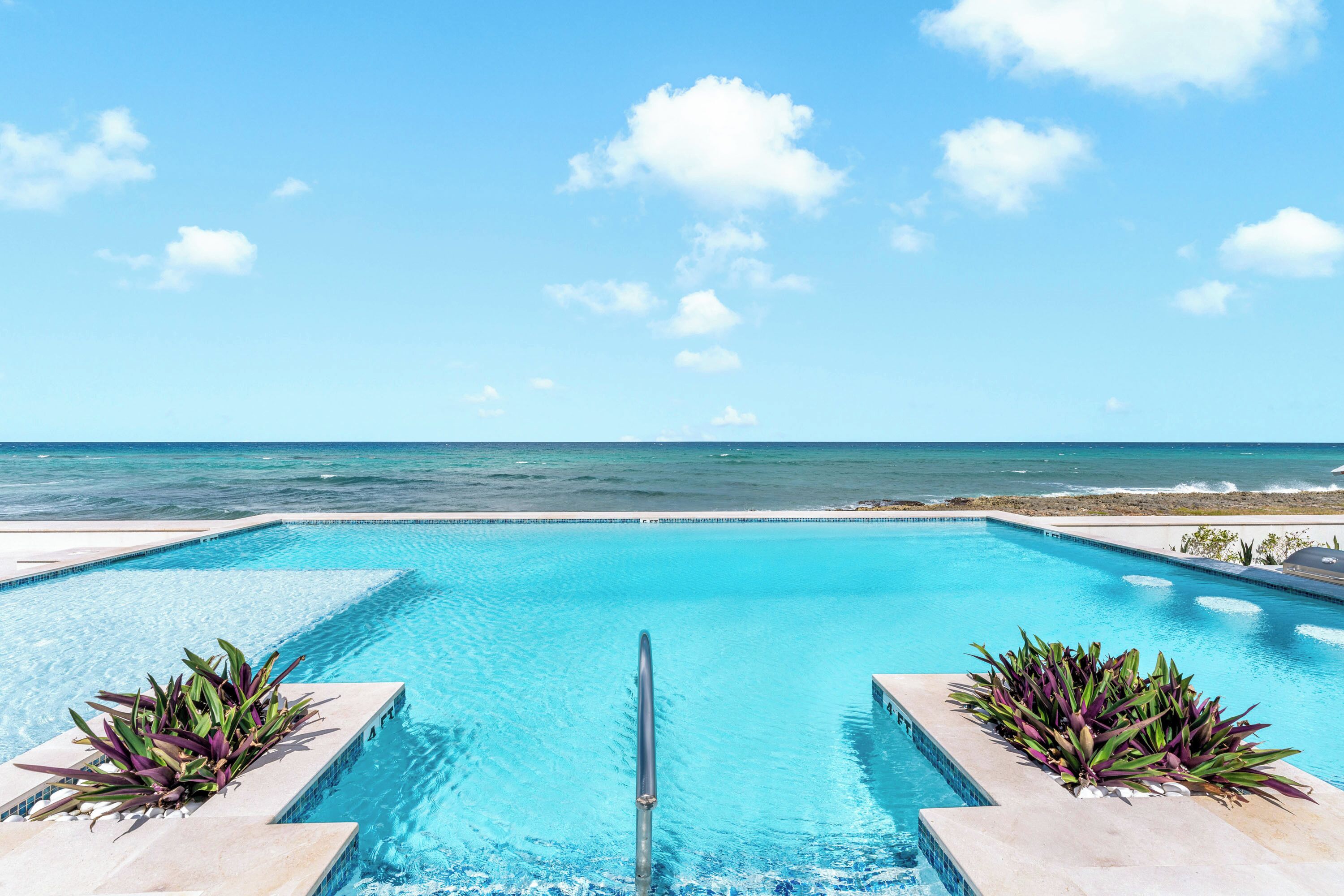 A rectangular swimming pool with clear blue water, surrounded by a tiled deck, and a view of the ocean.