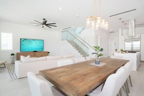 Ein modernes Wohnzimmer mit einem Holzesstisch, weißen Sofas, einem Fernseher und einer Treppe.