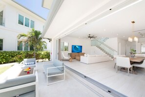A modern open-plan living area with a dining table, sofas, and a staircase. - Oceans 9: Seaside Lazy River Pool, Sunken BBQ Ocean Lounge + Designer Interiors in West Bay (Grand Cayman)