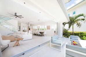 Een modern interieur met een trap, witte meubels, een eethoek en uitzicht op een palmboom.