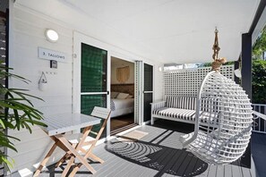 Ein Balkon mit weißem Tisch und Stühlen, einem Hängesessel und einem Bett, das durch eine offene Tür erkennbar ist.