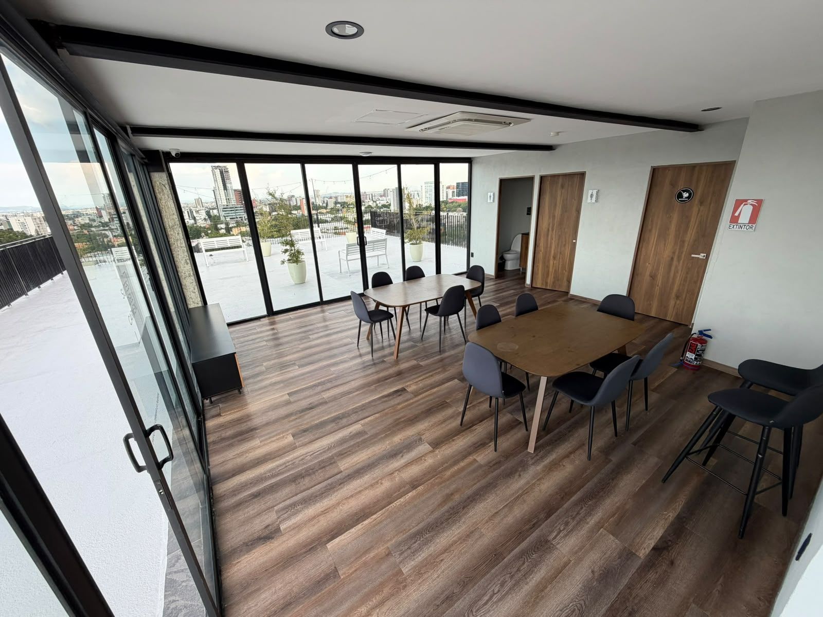 A modern meeting room with a large table and chairs, large windows with a city view, and a fire extinguisher on the wall.