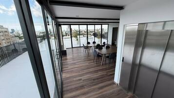 Een modern interieur met een grote glazen deur die uitkomt op een terras. Binnen ligt een houten vloer, staat een tafel met stoelen en is er een groot raam met uitzicht over de stad.