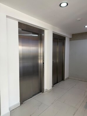 A hallway with two metallic elevator doors, white walls, and a tiled floor.