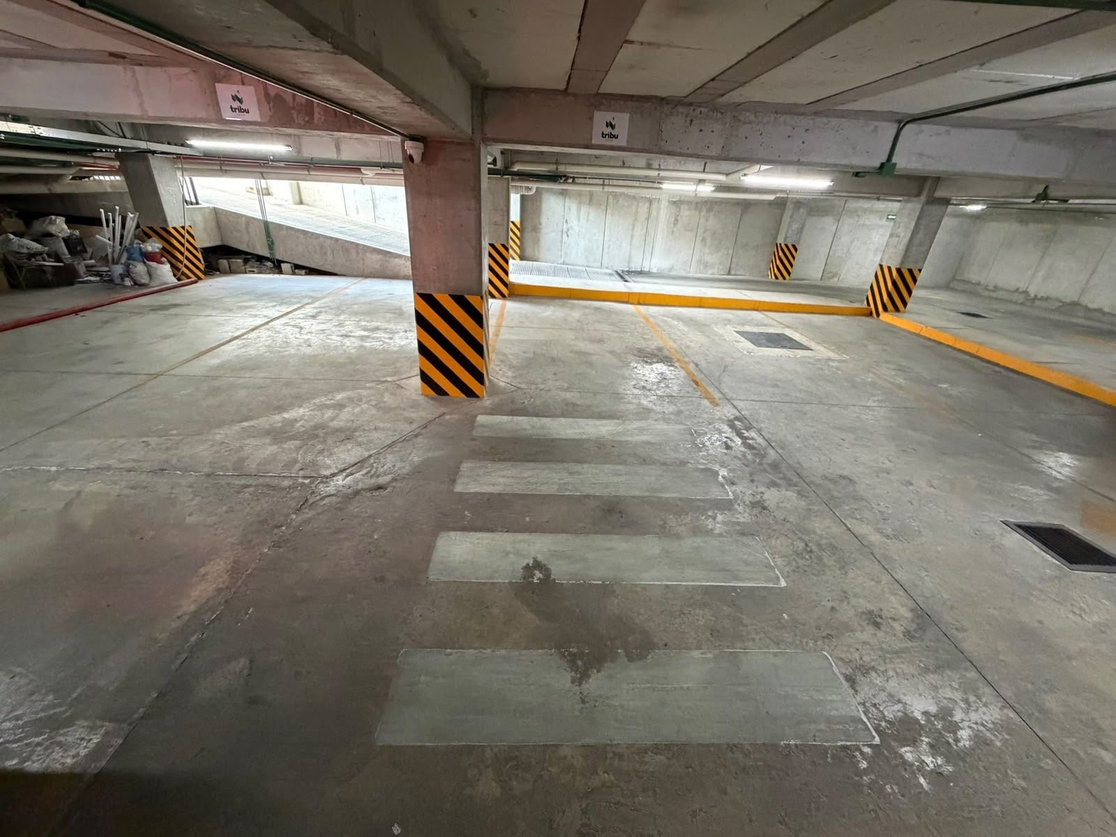 A parking garage with concrete pillars, yellow and black striped barriers, and a pedestrian crossing.