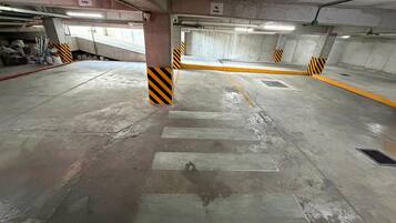 A parking garage with concrete pillars, yellow and black striped barriers, and a pedestrian crossing.