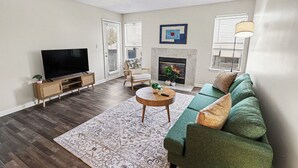 A living room with a flat-screen TV, a green sofa, a fireplace, and a patterned rug. - Bright/Spacious 2BR - King Bed/Pool/Gym Near UAB/Hospitals (Homewood)