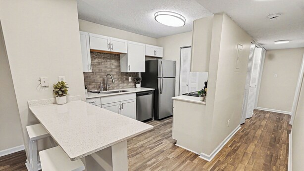 A kitchen with white cabinets, a stainless steel refrigerator, a dishwasher, and a wooden floor. - Bright/Spacious 2BR - King Bed/Pool/Gym Near UAB/Hospitals (Homewood)