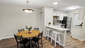 A modern kitchen with white cabinets, a stainless steel refrigerator, and a wooden dining table with chairs. - Bright/Spacious 2BR - King Bed/Pool/Gym Near UAB/Hospitals (Homewood)