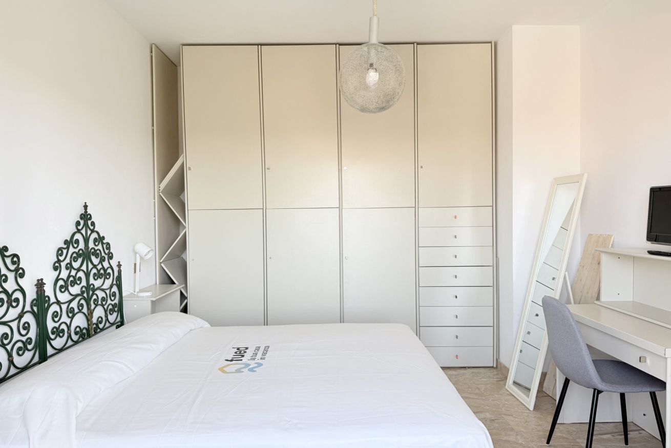 Une chambre à coucher comprenant un lit, un bureau, une chaise, une armoire et un luminaire suspendu.