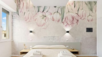 Une chambre à coucher avec un grand lit, une table de chevet, une lampe fixée au mur et une fresque murale à motifs floraux.