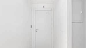 A white door with the number 102, a door handle, and a small red emergency button above it. - Essentia Boutique Rooms 102 – A comfortable break in central Cagliari ✨ (Cagliari)