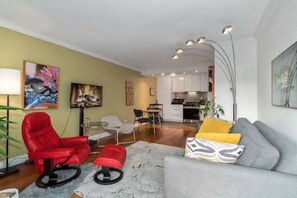 Ein Wohnzimmer mit einem roten Sessel, einem grauen Sofa mit gelben Kissen, einem Couchtisch und einer Stehlampe.