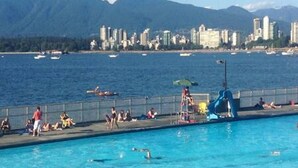 Una piscina con persone, uno scivolo e vista sul mare e sulle montagne sullo sfondo.