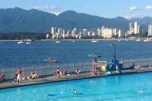 Ein Schwimmbecken mit Personen, einer Rutsche und Blick auf Meer und Berge im Hintergrund.