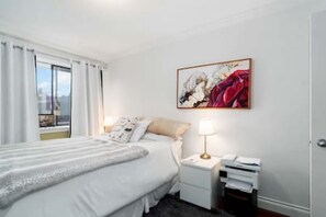 Ein Hotelzimmer mit Bett, Nachttisch mit Lampe, einem Bild an der Wand und einem Fenster mit Vorhängen.