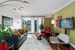Ein modernes Wohnzimmer mit einer Couch, Sesseln, einem Fernseher und einem Balkon.