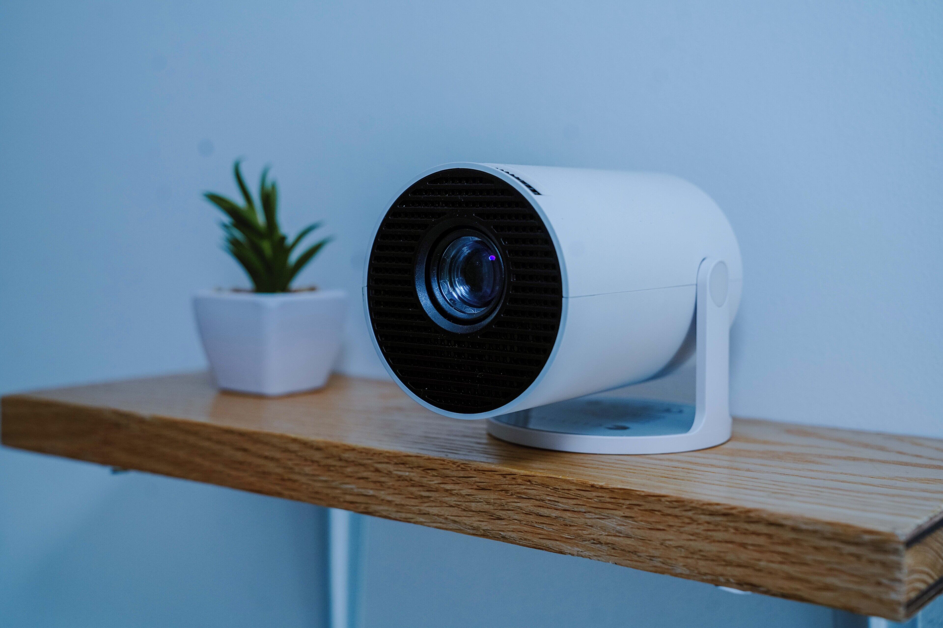 A webcam on a wooden shelf with a potted plant beside it.