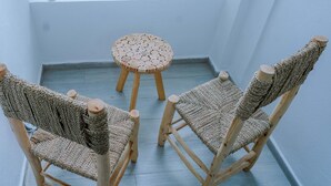 Un balcón con dos sillas de madera y una pequeña mesa redonda, con vista a una calle con coches estacionados.