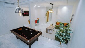 Una sala de estar moderna con una mesa de billar, un sofá verde y una planta en maceta.