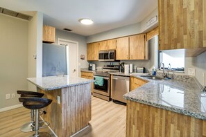 A kitchen with wooden cabinets, stainless steel appliances, a granite countertop, and a bar stool.