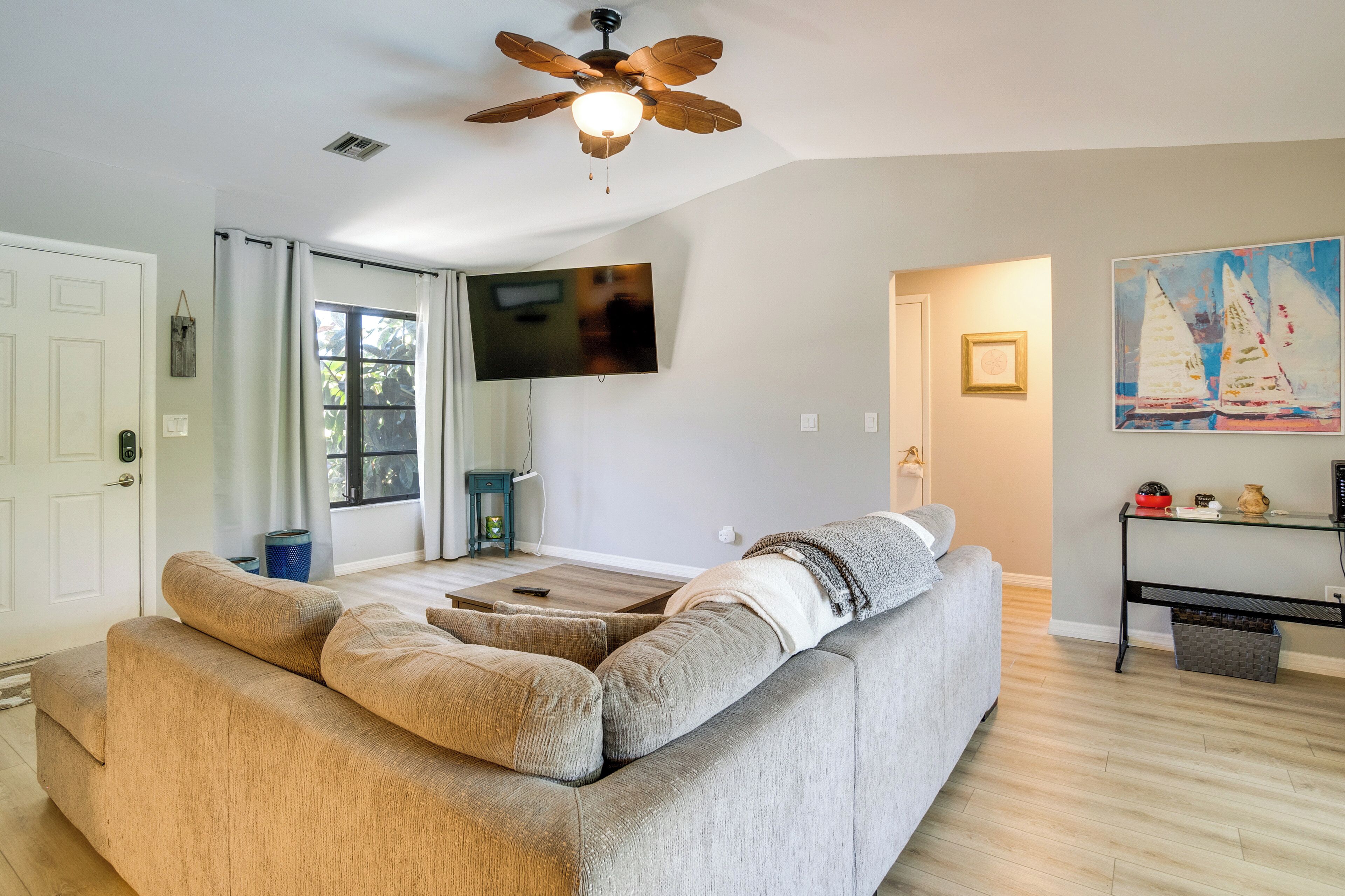 A living room with a sectional sofa, a ceiling fan, a flat-screen TV, and a sailboat painting.
